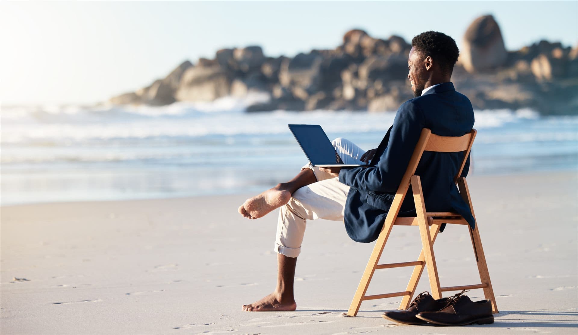 Broker profissional trabalhando com laptop na praia, de pés descalços